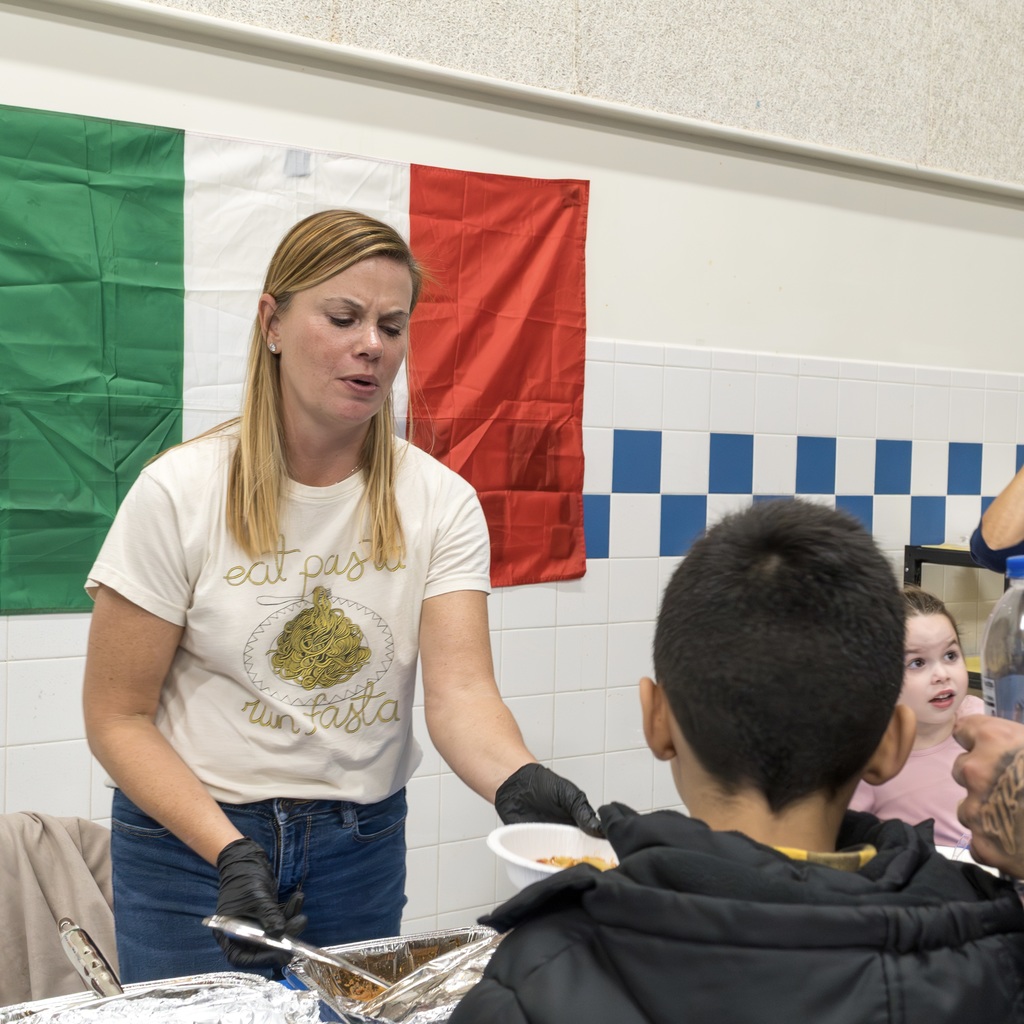 A Richer School staff member representing Italy hands out pasta to students and families.