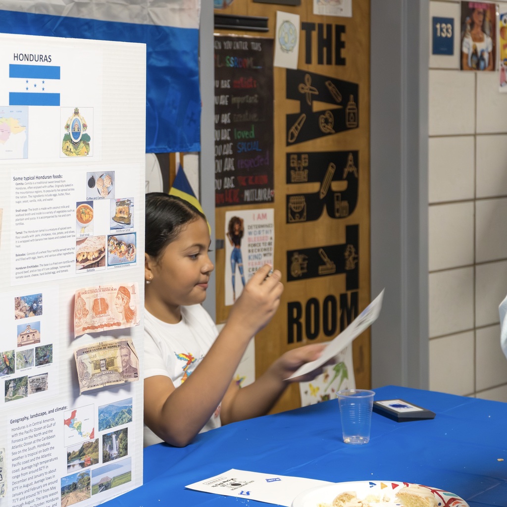 A Richer School student representing Honduras sits at a table reading from a piece of paper.