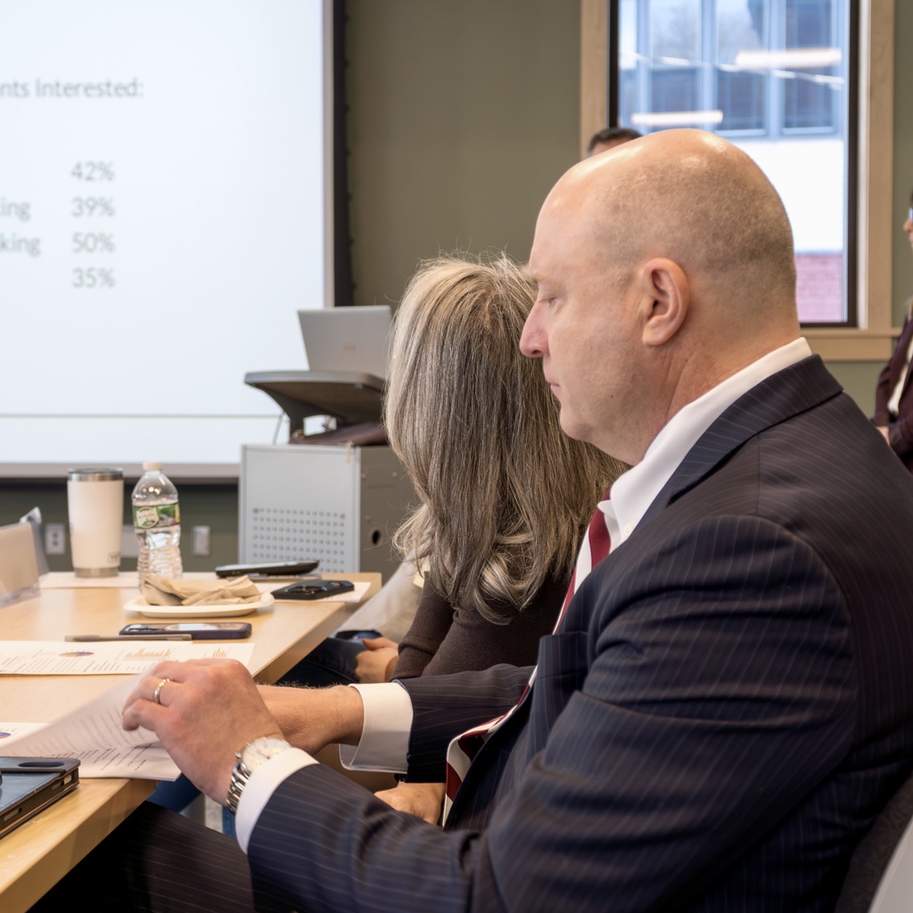 An MEDC board member sits at a table, looking at a document, during an MHS presentation at the library.