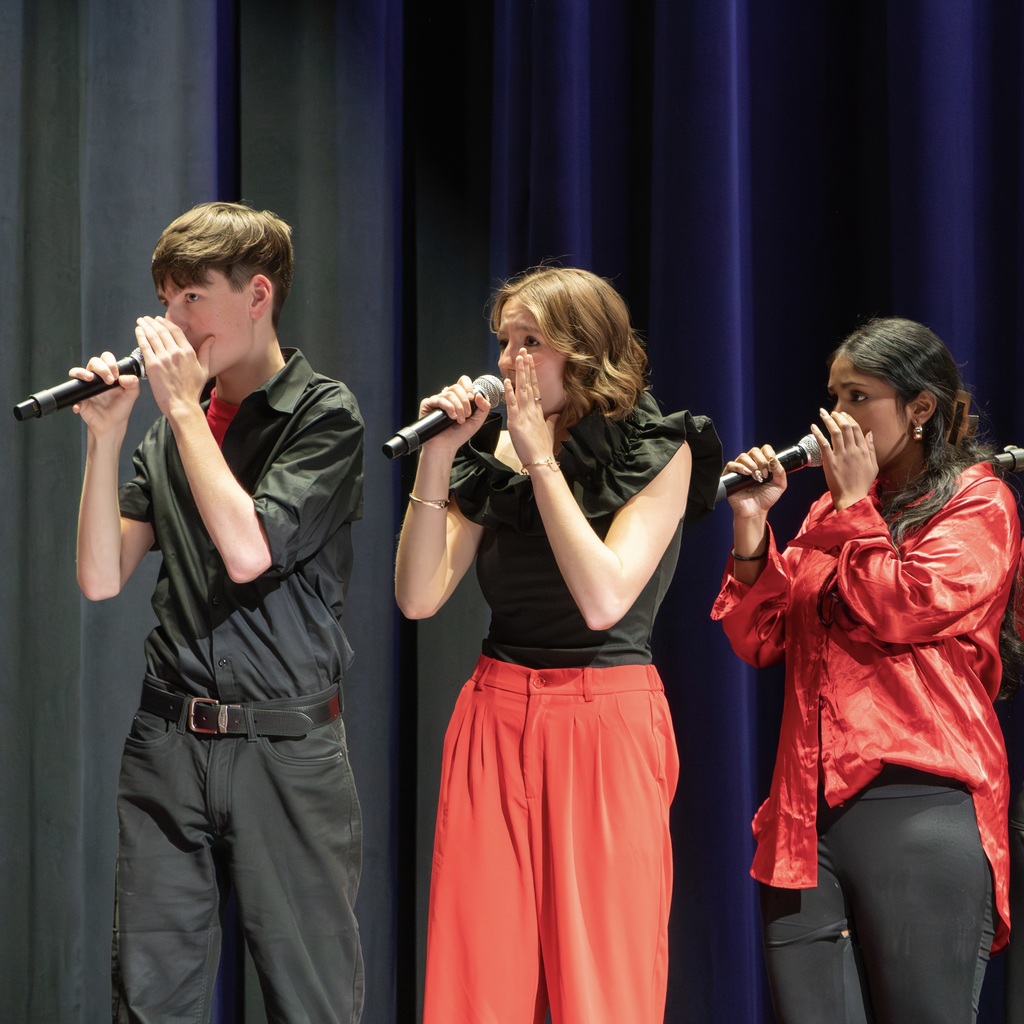Three The Thursdays members sing, looking right as they cover their mouths with their left hands.