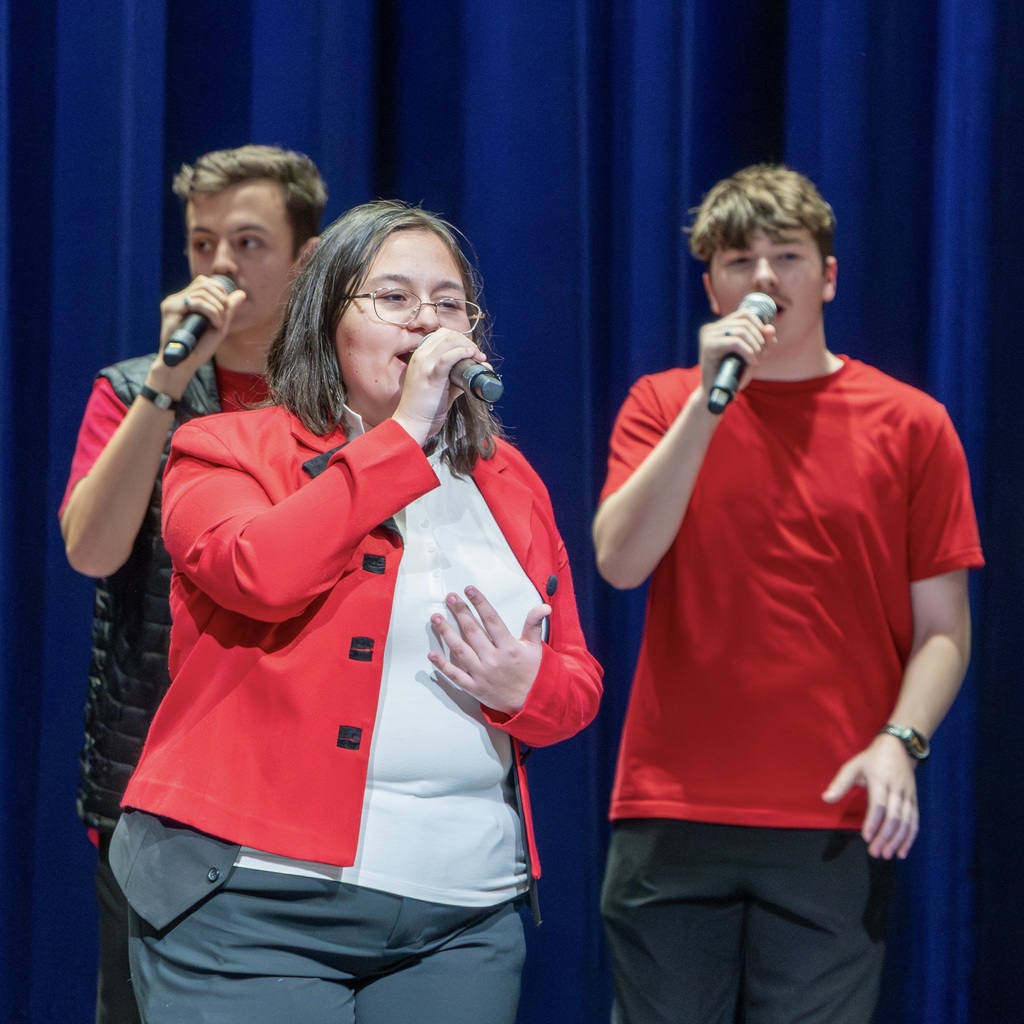 Three Voices Rechoired members sing on stage.