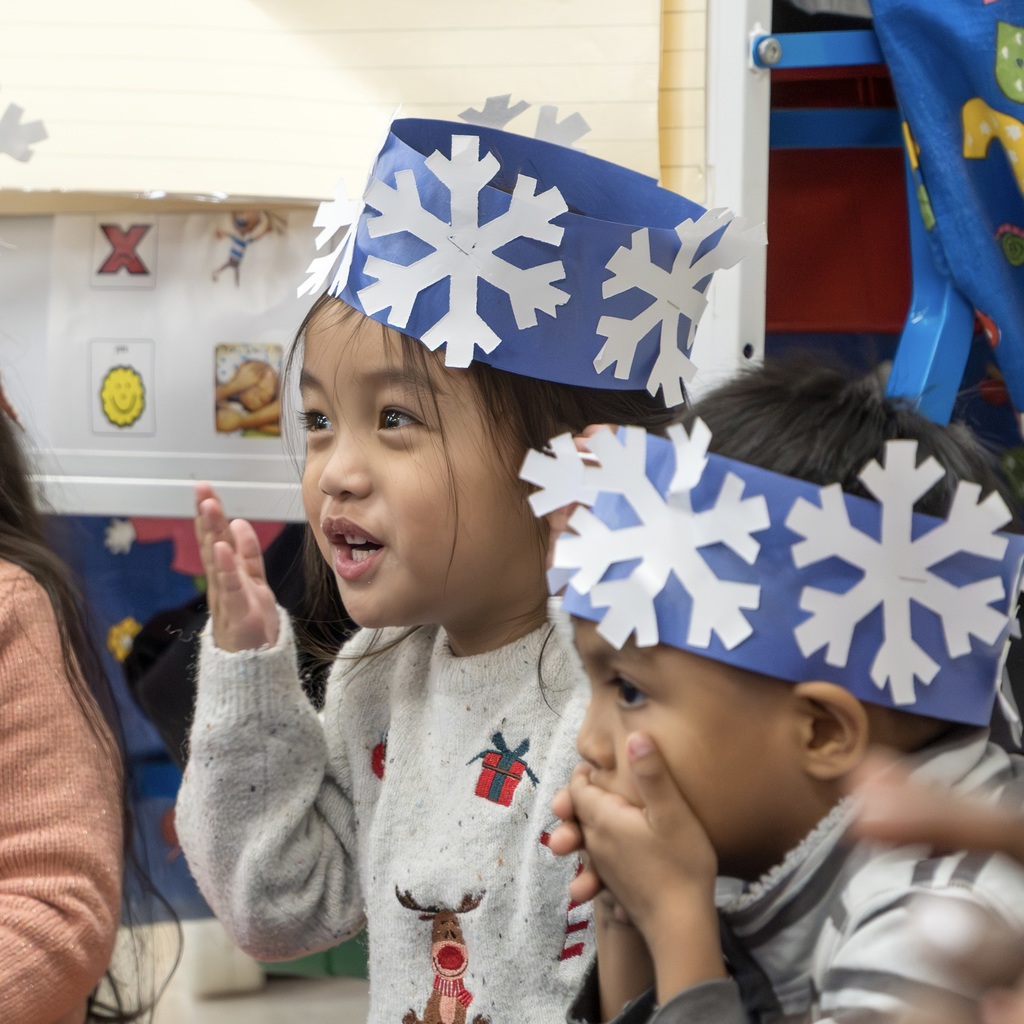 Two students wearing blue paper crowns with snowflakes on them give out air kisses.