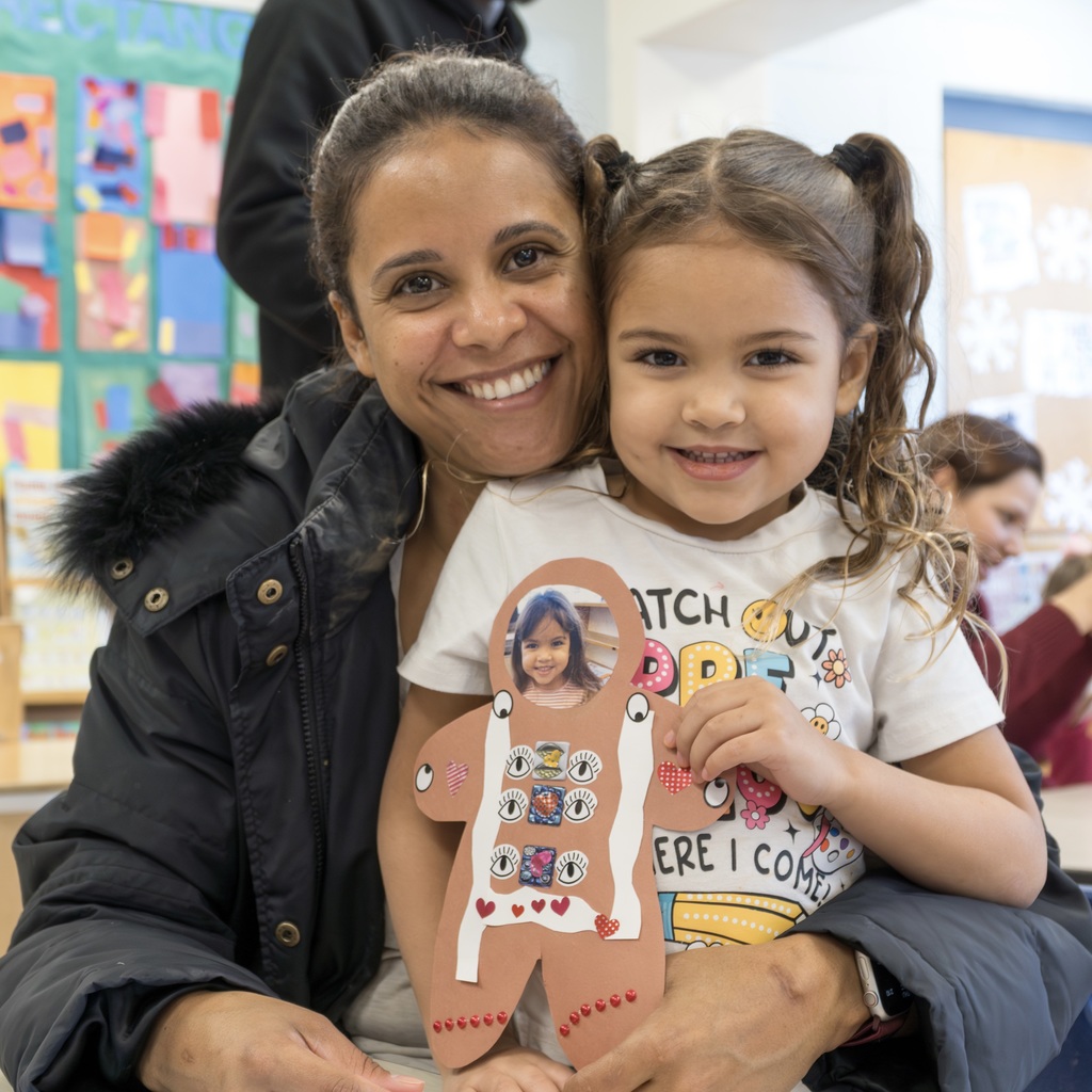  A mom holds her daughter in her lap, smiling at the camera. The girl, an ECC student, holds on to her gingerbread man craft.