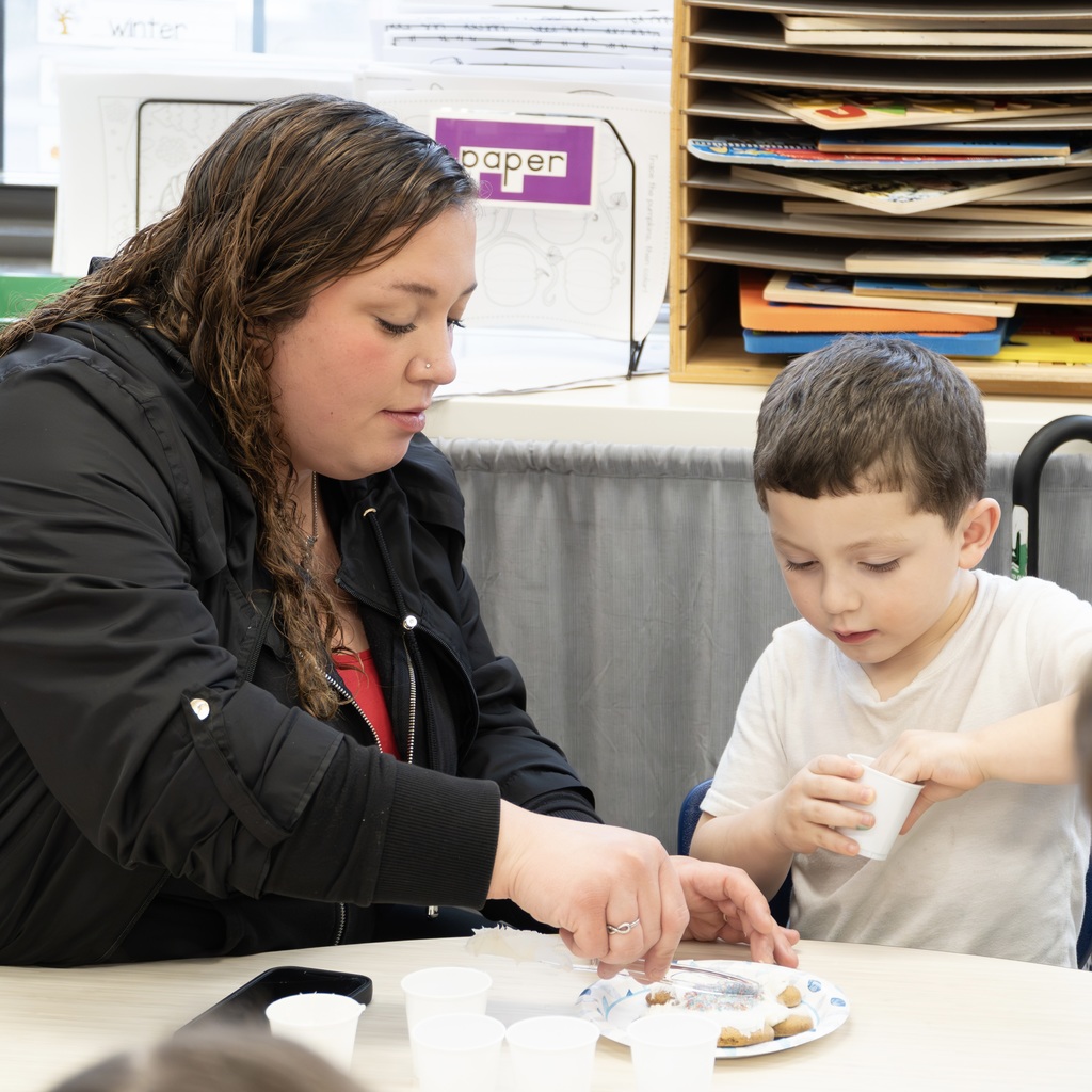An ECC student and his mom sit down at a table to work on a craft together.