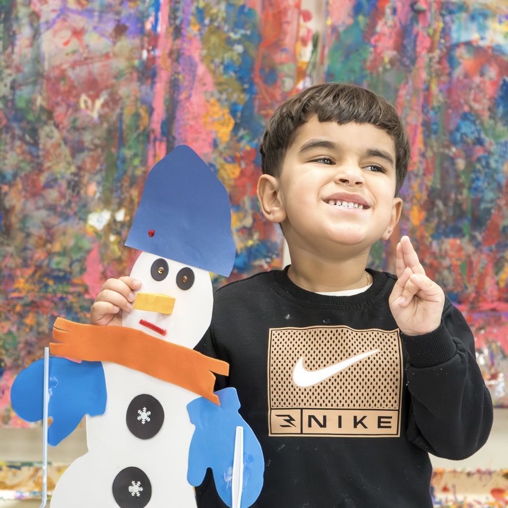 An ECC student smiles and throws up a peace sign as he poses with his snowman craft.