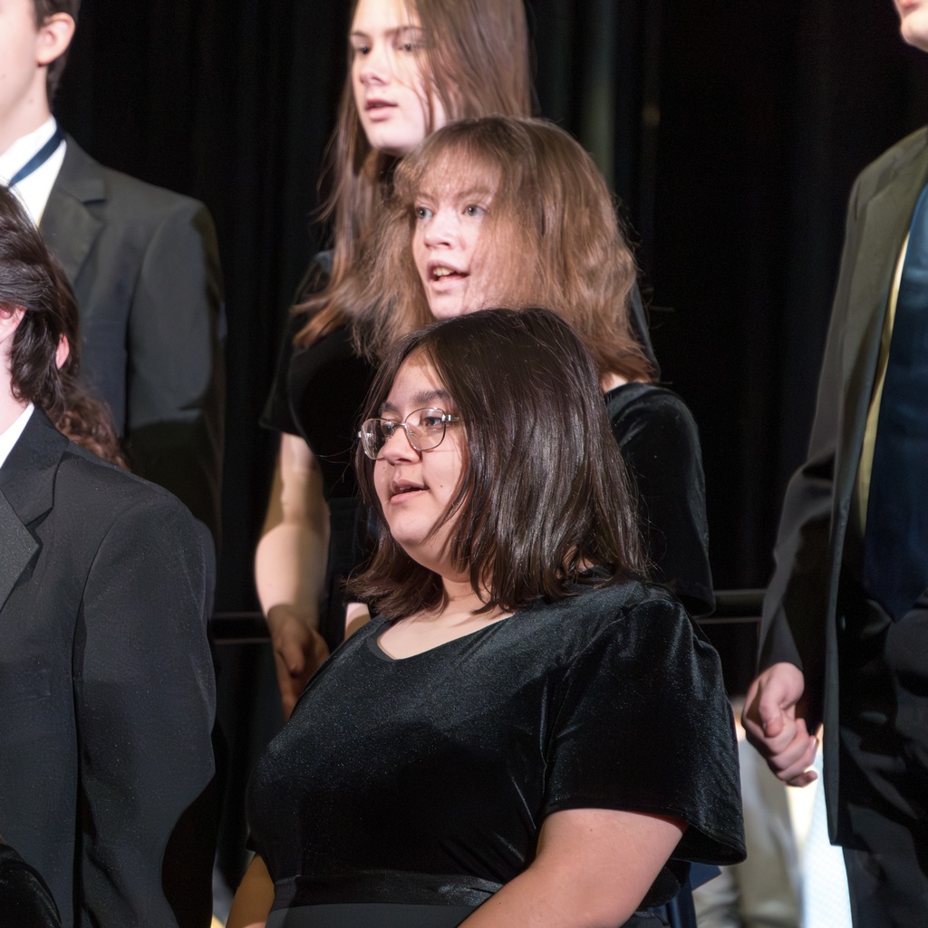 Three female Voices ReChoired members stand on a riser, singing.