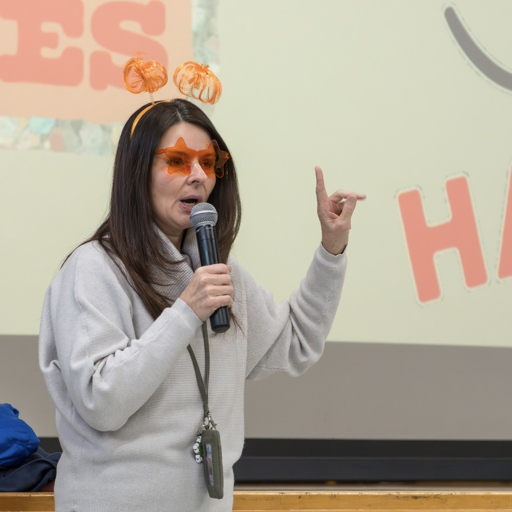 Richer School principal Lisa Richards uses a microphone to speak. Her left pointer finger is up in the air.
