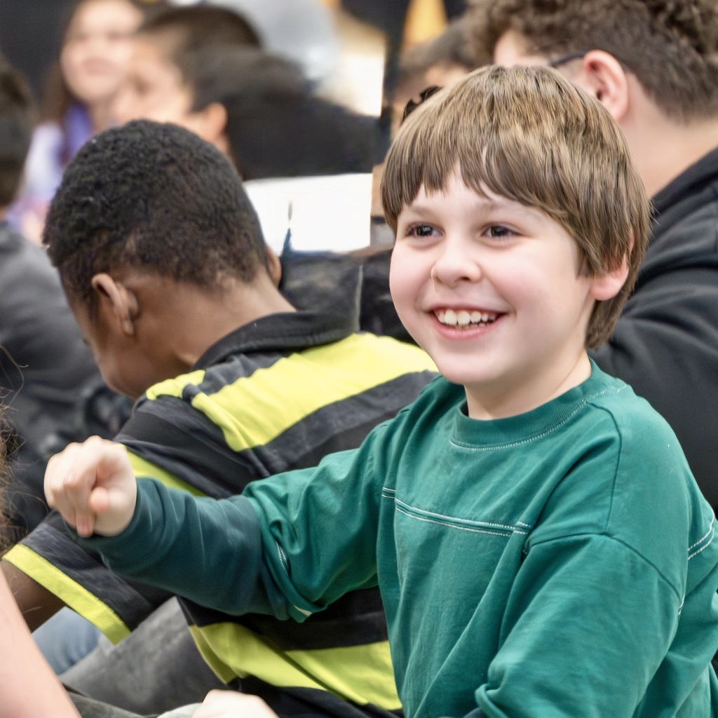 A Richer School student wearing a green sweater sits in a crowd of students, smiling.