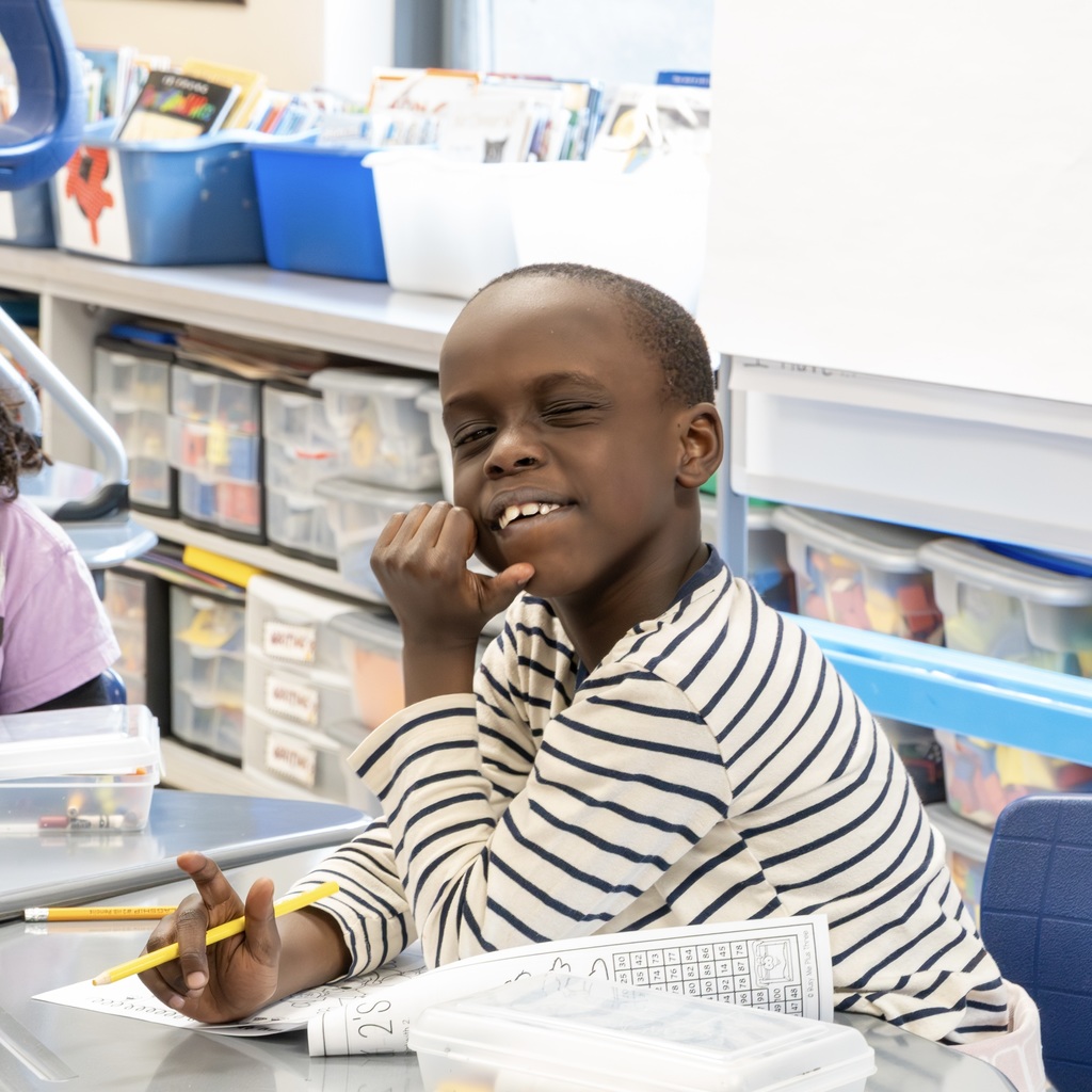 A Jaworek School student sitting down at a desk winks at the camera.