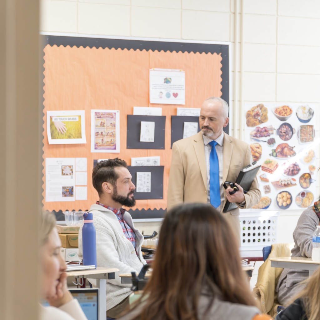 Superintendent DeFalco stands looking down towards Assistant Superintendent Skaza, who is sitting.