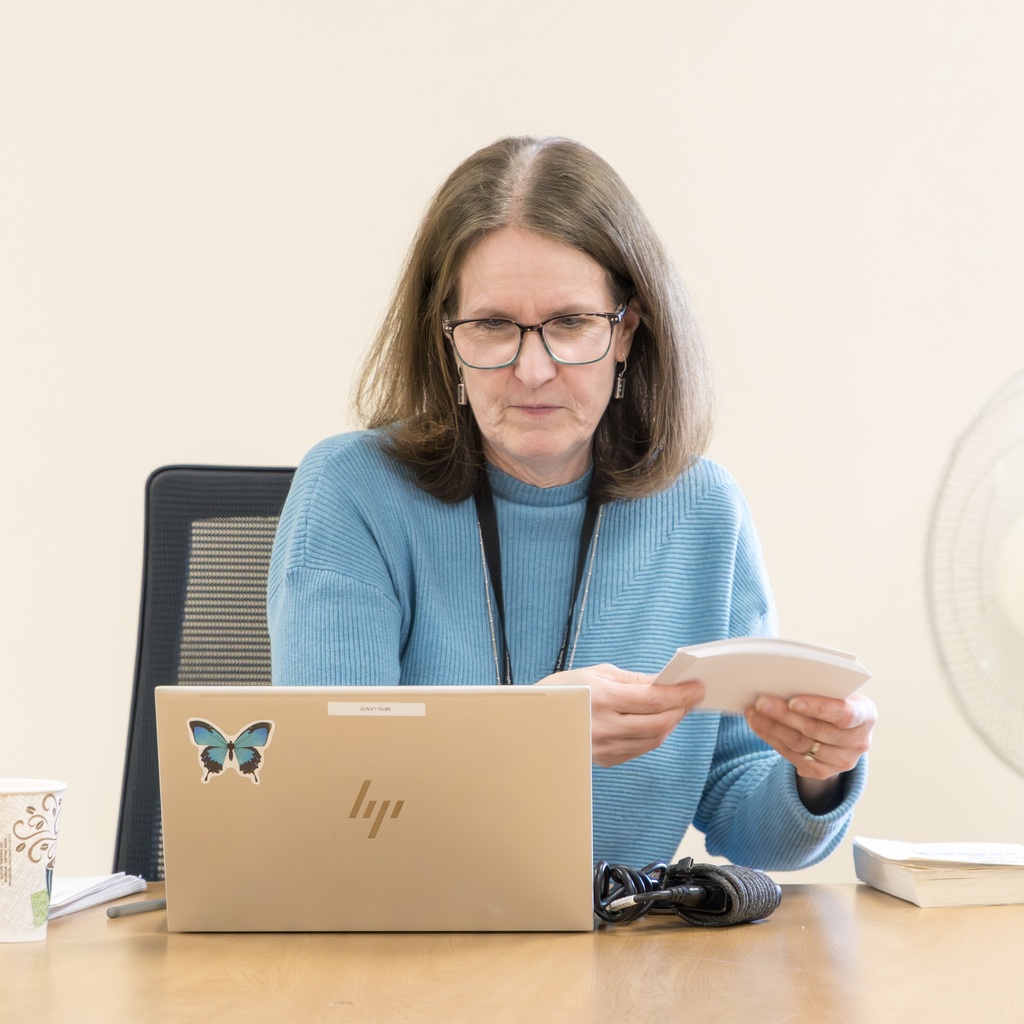 HR Director Patty Brown sits, holding a stack of index cards as she looks down at her laptop.