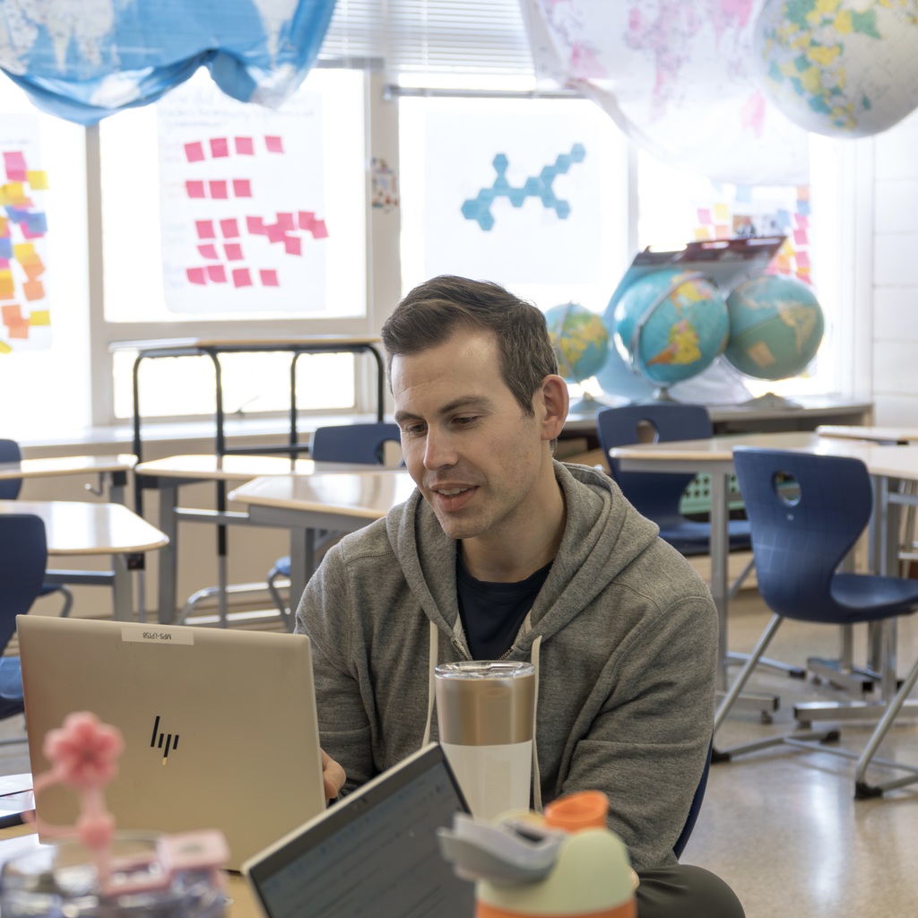 A male faculty member sits at his desk working on his laptop.