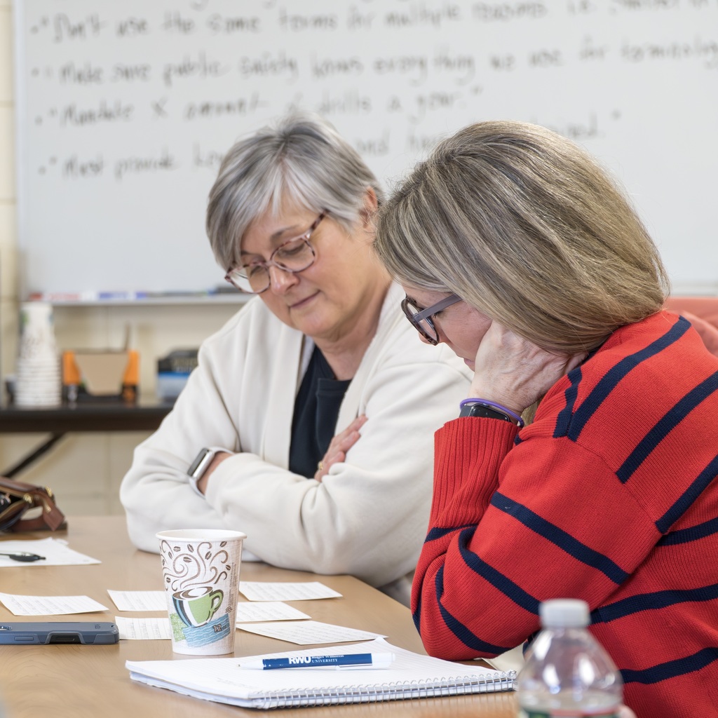 Two faculty members sit at a table, reading index cards.
