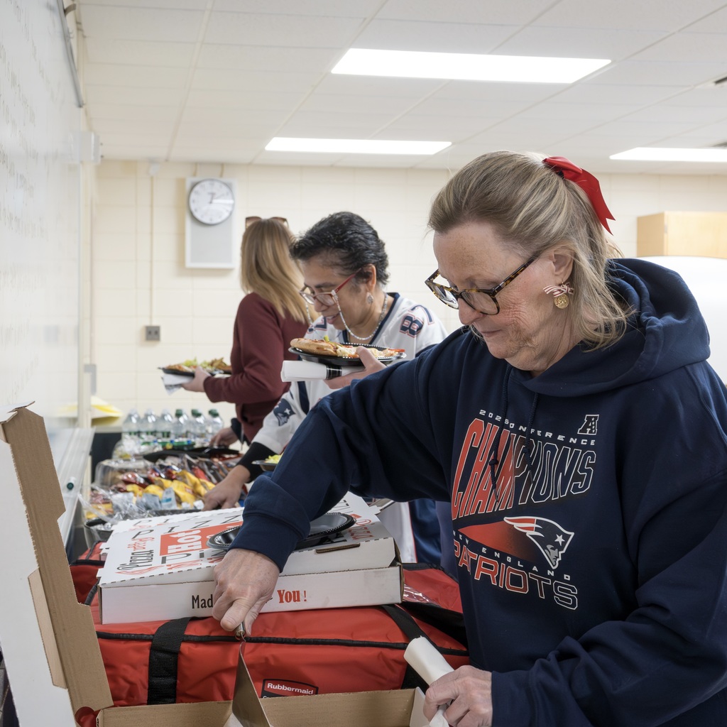 Two finance team members wearing Patriots gear serve themselves from a buffet table in a conference room.