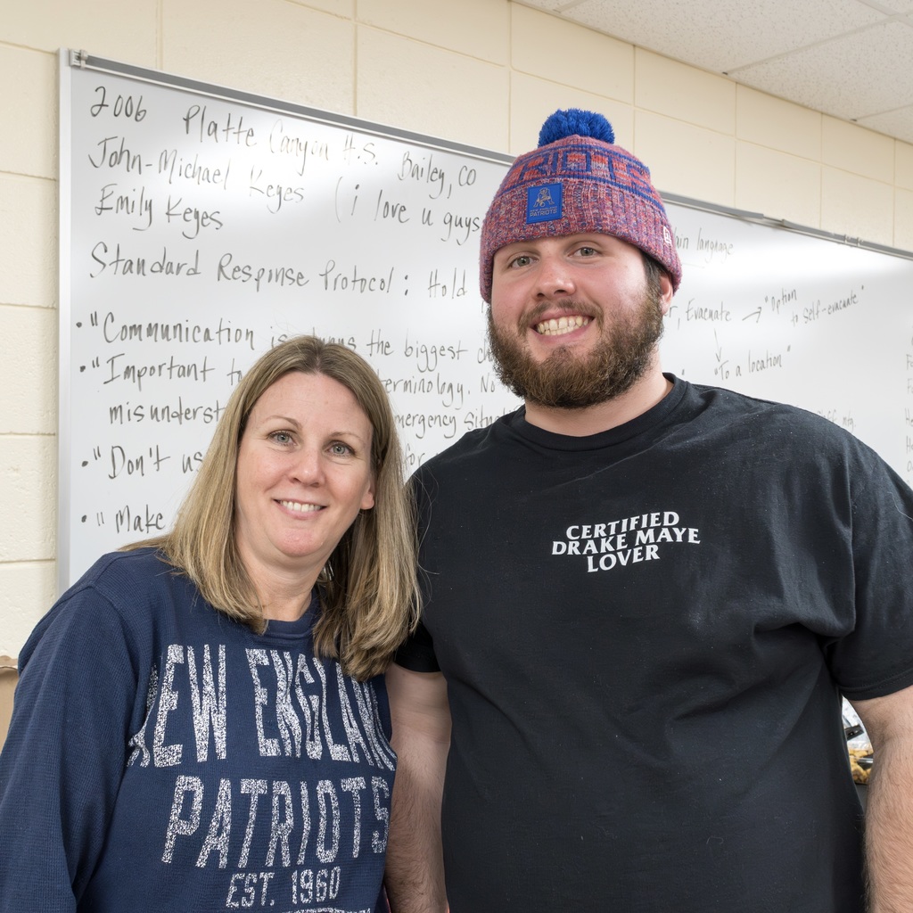 Two MPS staff members wearing Patriots gear smile for a group photo.