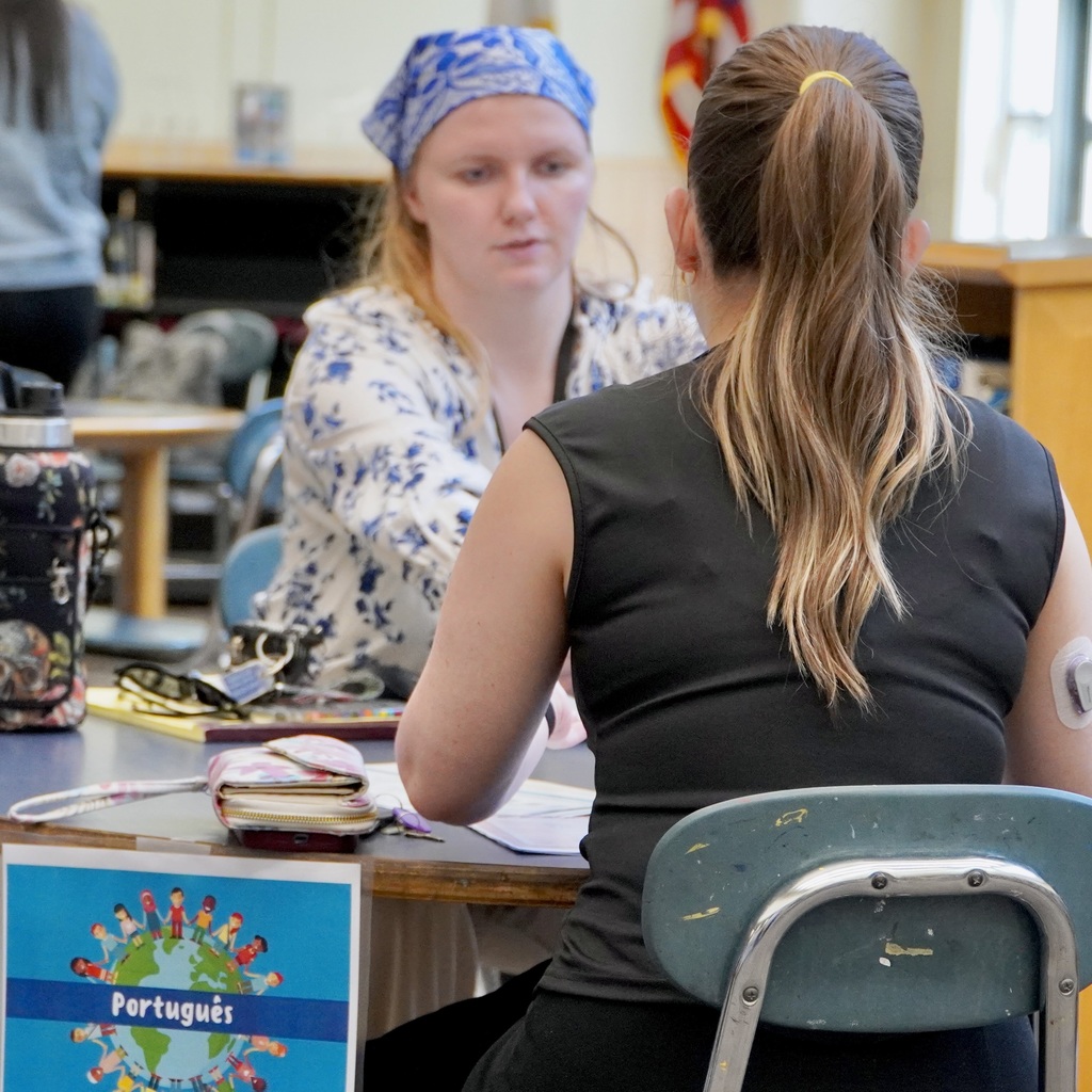 A Portuguese interpreter sits down at at able with a parent at a kindergarten registration workshop.