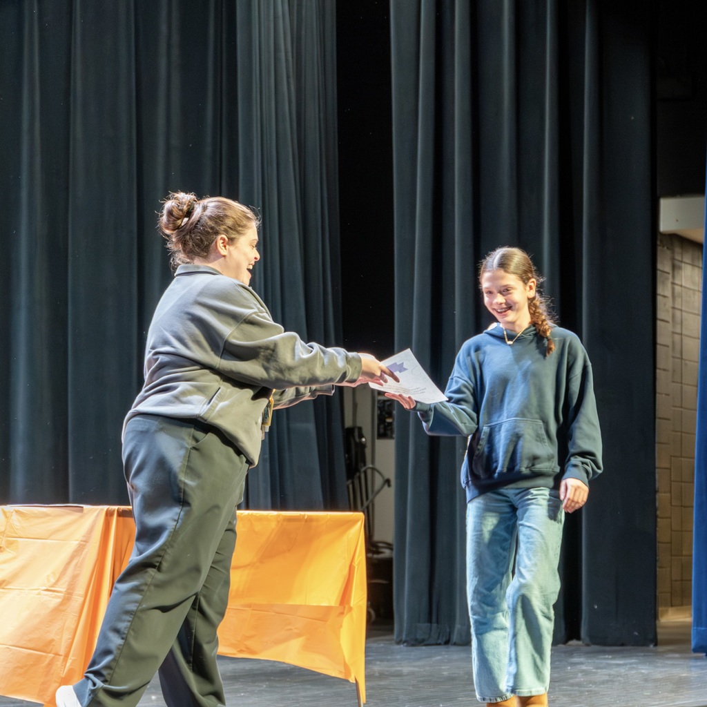 A staff member hands a certificate to a female student on the Whitcomb auditorium stage.