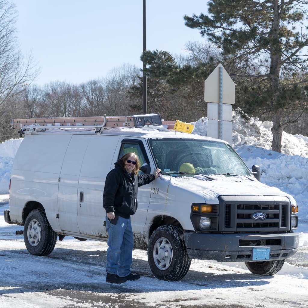 An MPS facilities member stands next to a white van outside a snow-covered parking lot.