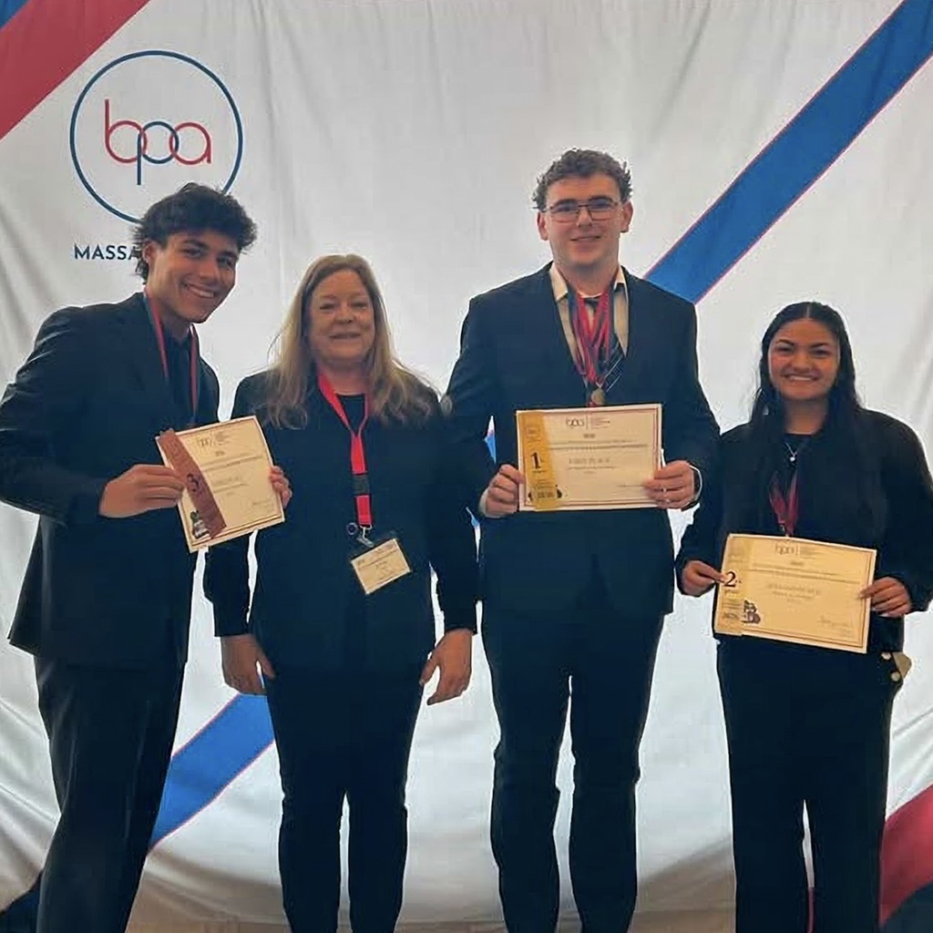 Three MHS BPA Club members and their club adviser in formal attire stand in front of a backdrop. Each student holds a certificate. The backdrop features red, white, and blue colors.