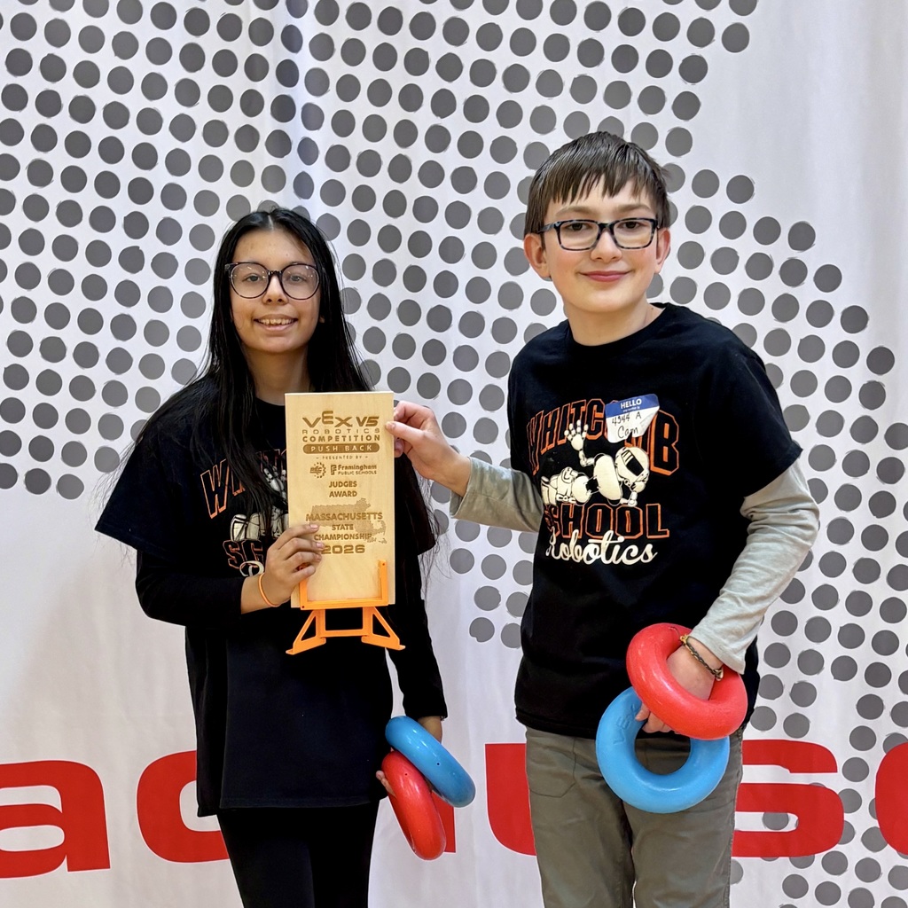 Two kids, one holding a certificate and the other two rings, stand next to each other with a patterned wall behind them.
