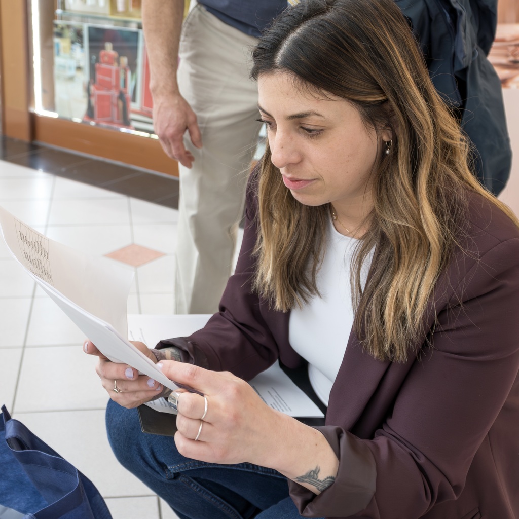 MHS Career Specialist Jackie Coyle, with long hair, is squatting on the floor, studying a paper. A person stands behind her.