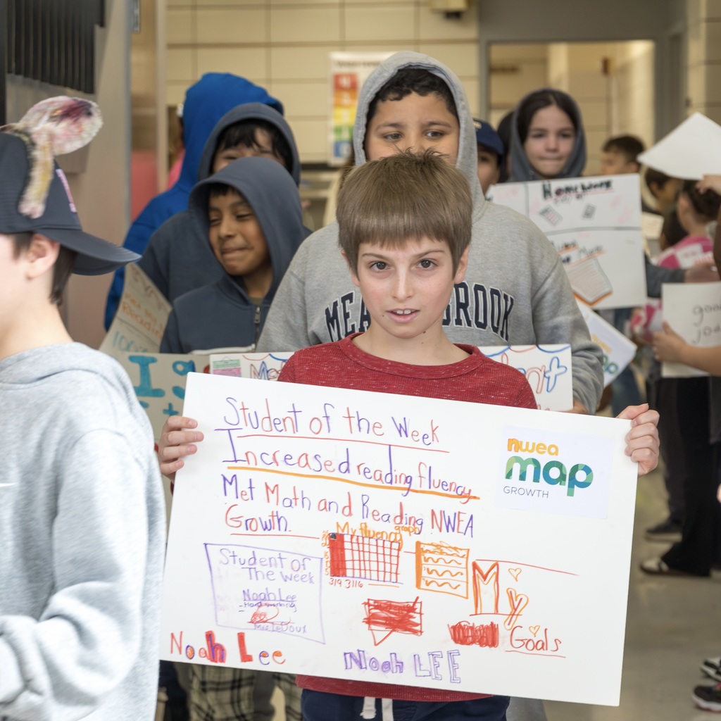 Several students stand in a hallway, one holding a sign that reads "Student of the Week".