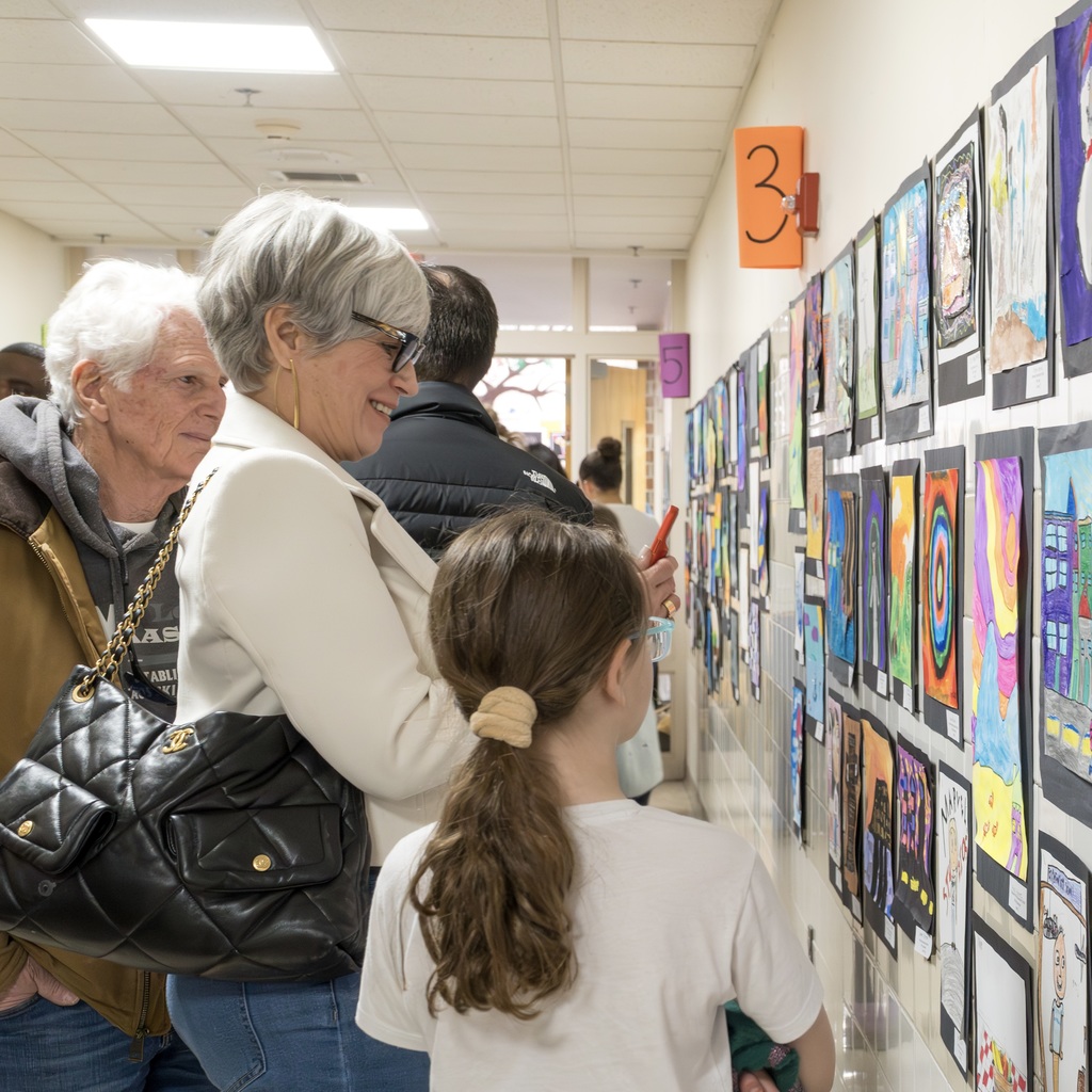 A hallway with artwork on the wall, with a woman in glasses and a girl with a ponytail.