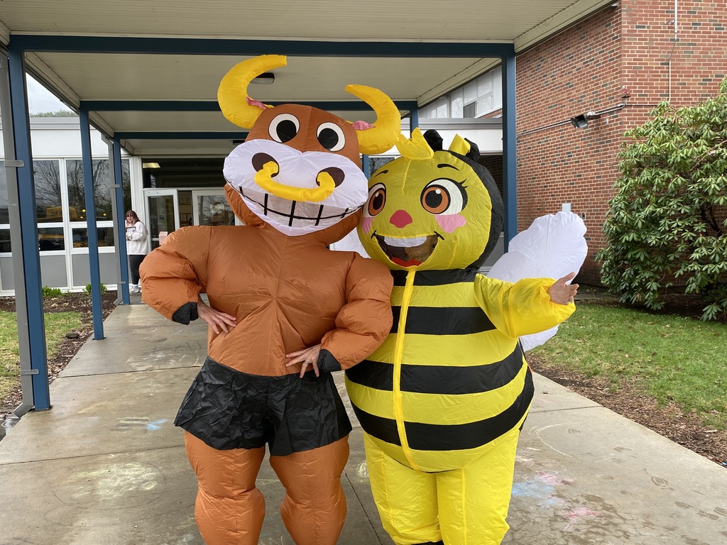 Two people, one in a cow costume and the other in a bee costume, stand together on a sidewalk.