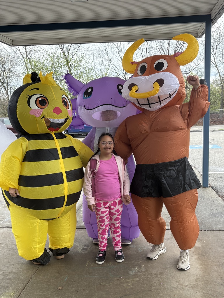Four people stand together in front of a building. One girl and three mascots, including a bee, a cow, and a bull.