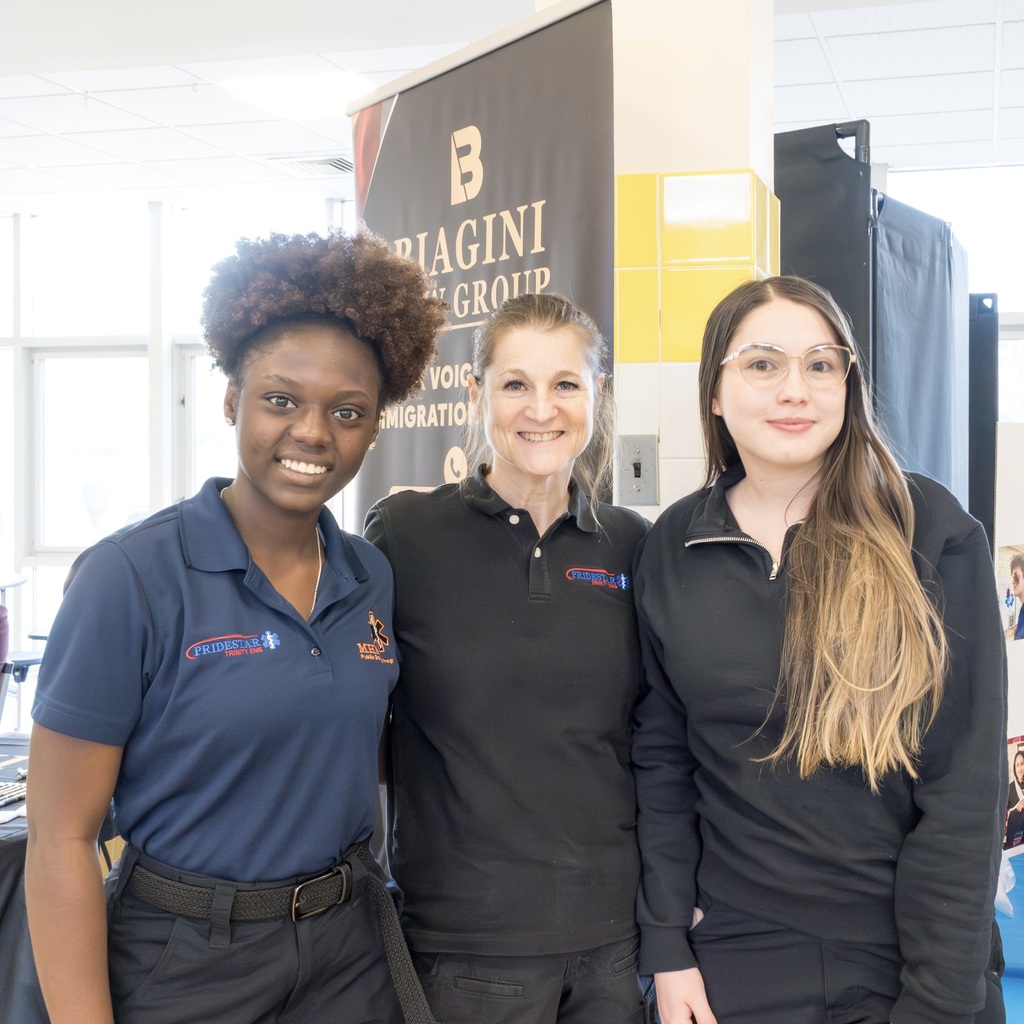 Three women in uniform, standing together with smiles. The woman on the left wears a blue polo shirt, the woman in the middle wears a black shirt, and the woman on the right wears a black jacket.