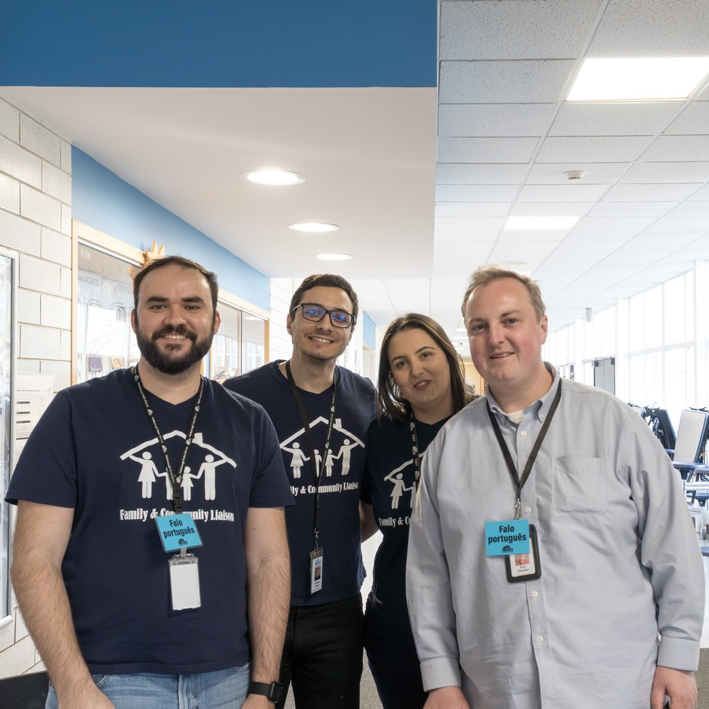 Four MPS staff members stand in a hallway; three wear ID cards and one wears a long-sleeve shirt.