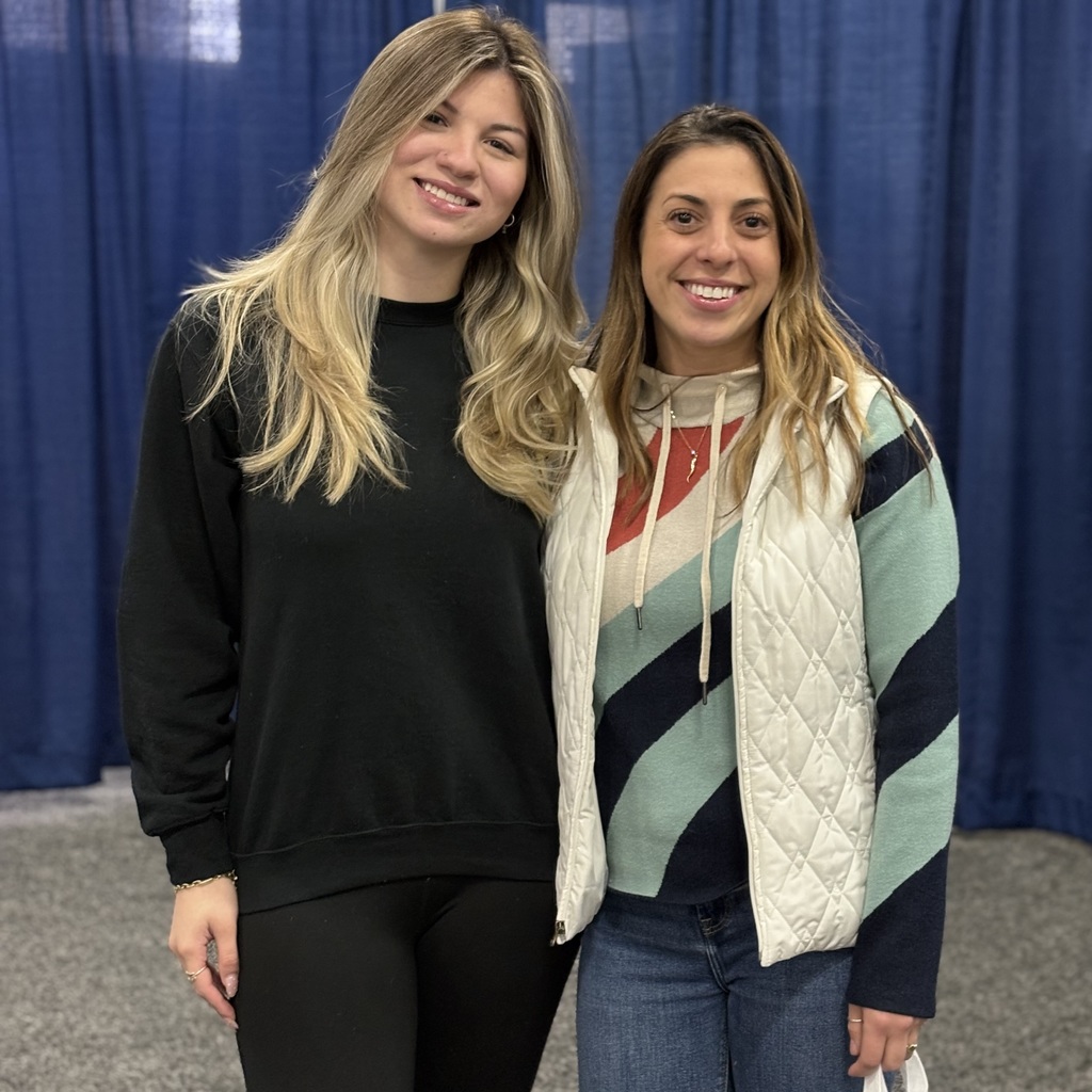 MHS Career Specialist Jackie Coyle and an MHS alum, one in black and one in a striped jacket, standing next to each other in front of blue curtains.