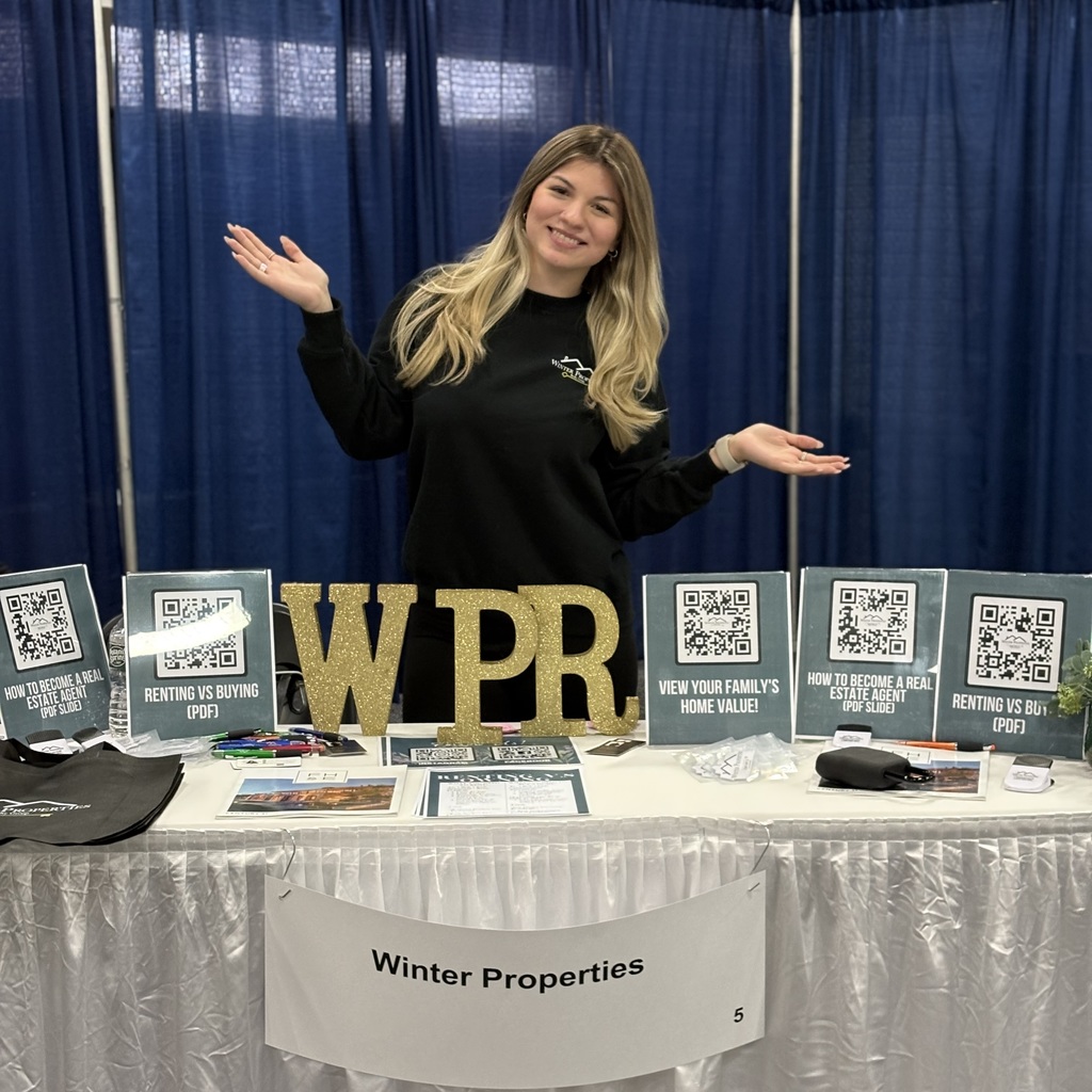 An MHS alum stands at a table with a sign reading "Winter Properties" and "WPR" letters in front.