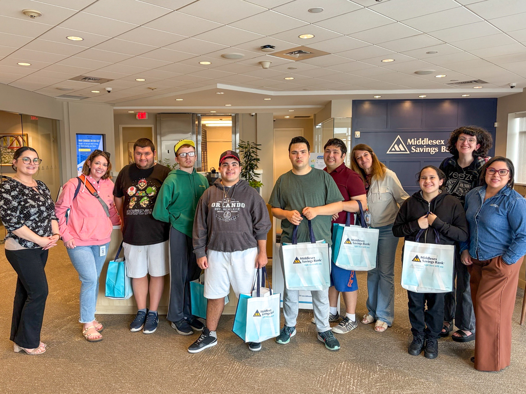 A group of LIFE program participants and staff stand in a hallway, holding bags, with a blue sign in the background.
