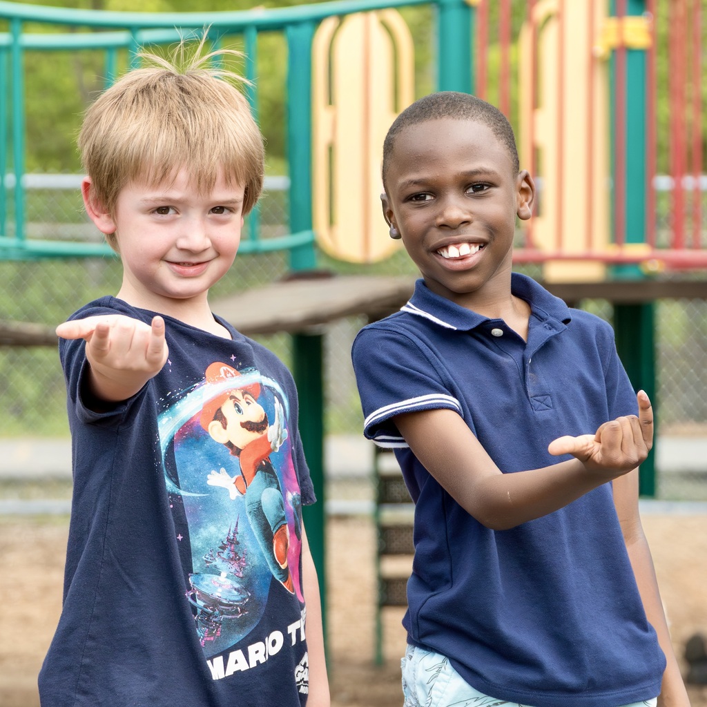 Two boys, one in a Mario shirt, the other in a blue polo, stand in a playground.