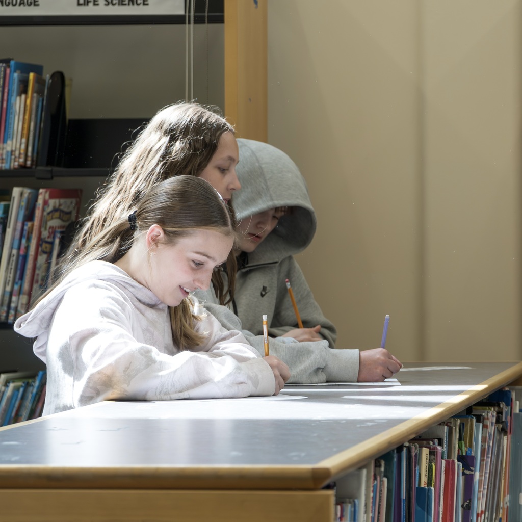 Three students leaning over a bookshelf, writing.