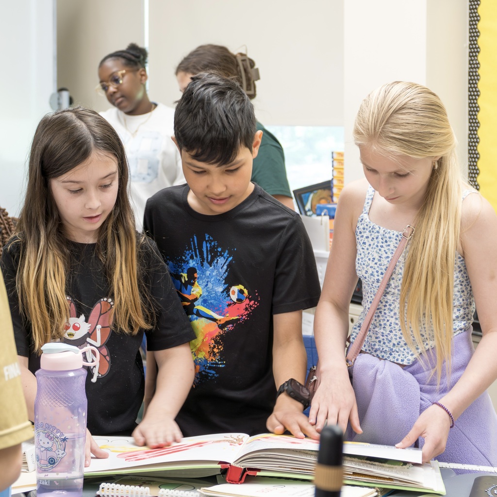 Three Jaworek students examine an open book on a table in a classroom.