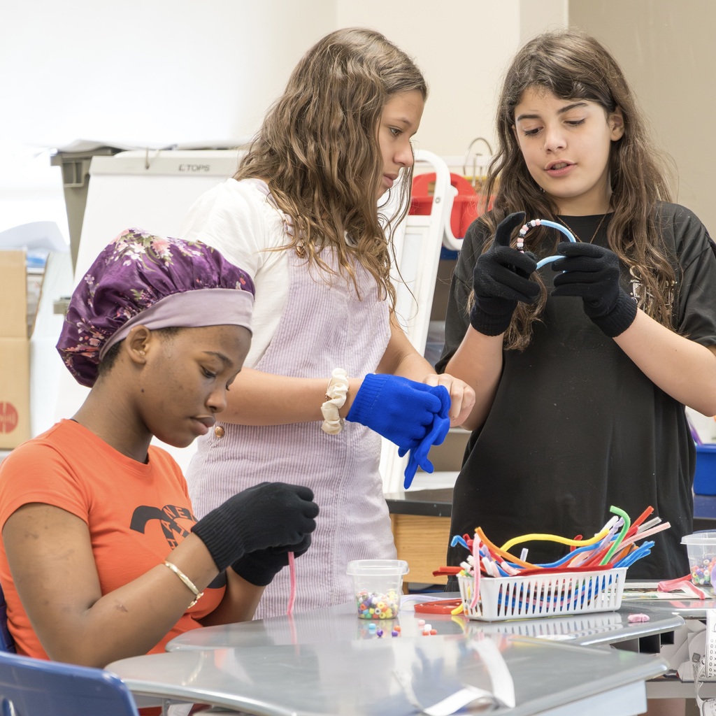 Three Jaworek students in a classroom; one in a purple cap works on a project at a table.