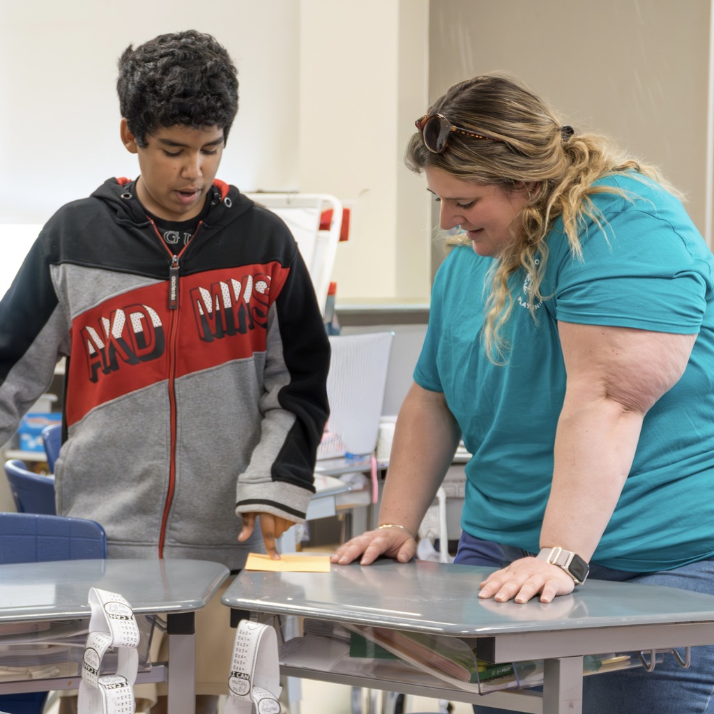 A Jaworek staff member in a teal shirt and a boy in a black, red and gray jacket stand at a table.