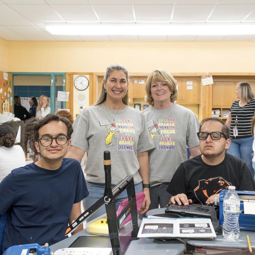 Four individuals in a classroom setting, with two MPS staff members and two students wearing t-shirts with colorful graphics.