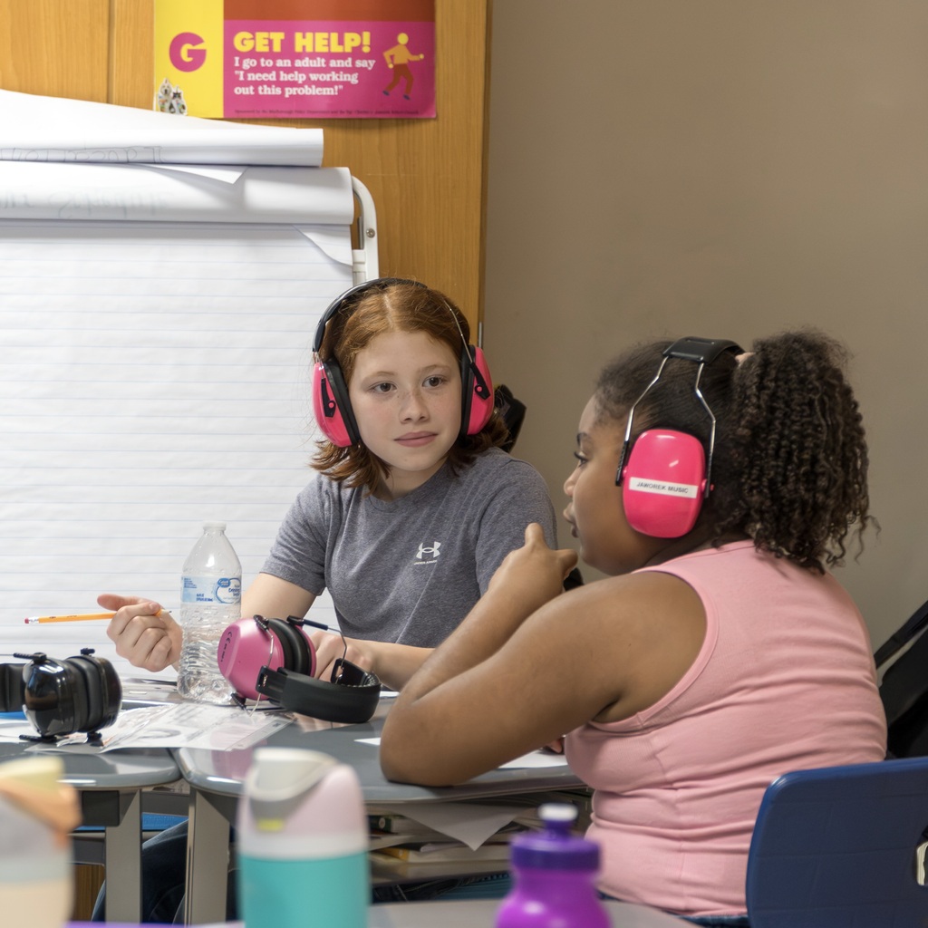 Two young Jaworek girls, with pink headphones, sit at a table in a classroom.