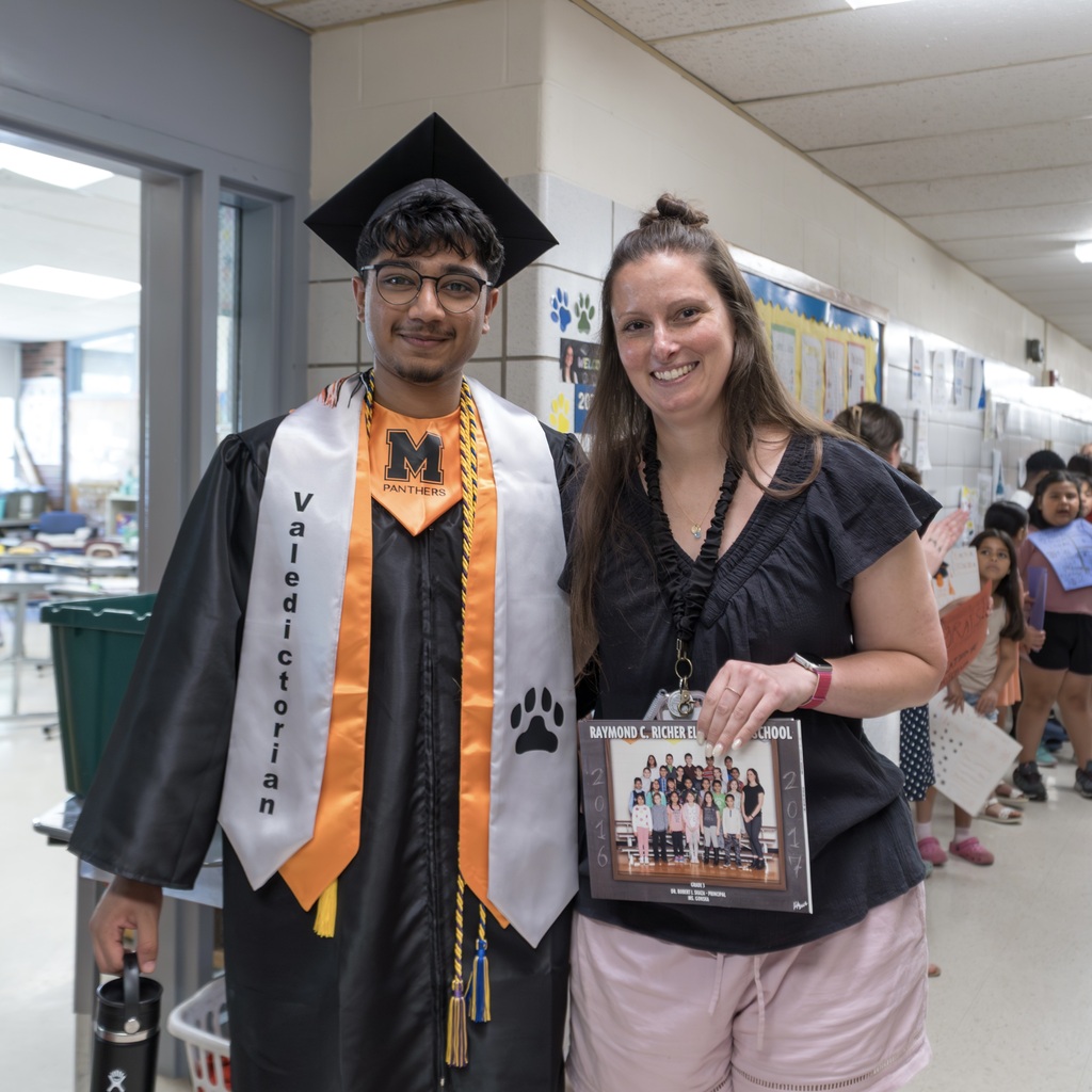 The MHS Class of 2026 valedictorian, in a graduation gown, stands next to a smiling woman holding a framed photo.