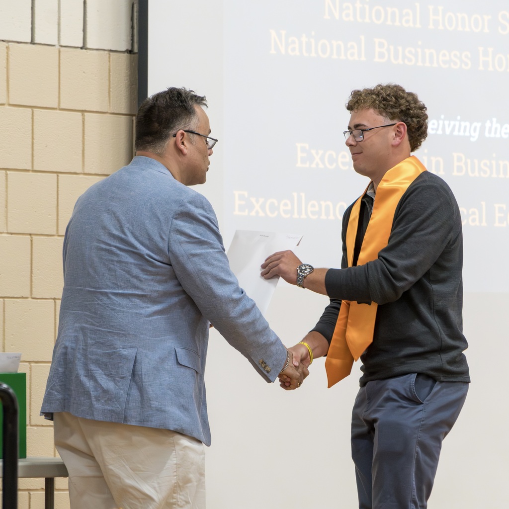 An MHS staff member, in blue, and an MHS male student, in black, stand facing each other in front of a projector screen.