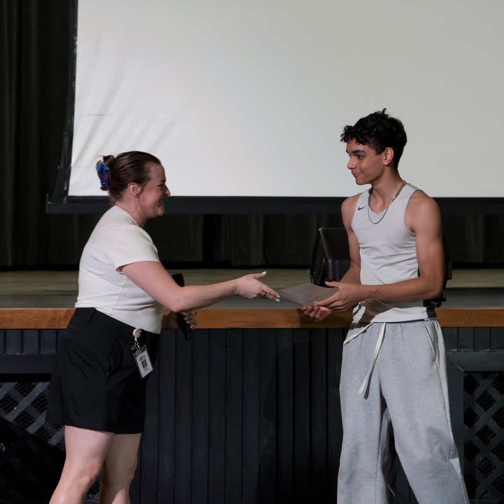 A Whitcomb female teacher and a young male student are on stage, the woman holding an award and presenting it to the young man.
