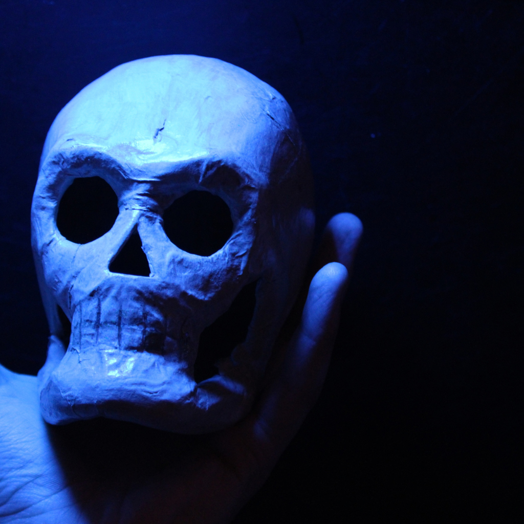 A hand holds a white skull model with hollow eyes and a wide mouth under a blue light.