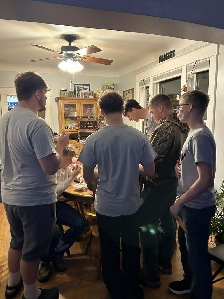 Several Red Raiders football players stand and sit around a dining table, sharing food and conversation during their team-building dinner.