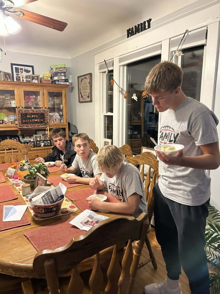 Four Red Raiders football players sit around a wooden dining table, enjoying dessert from bowls while visiting together in a home decorated for Halloween.