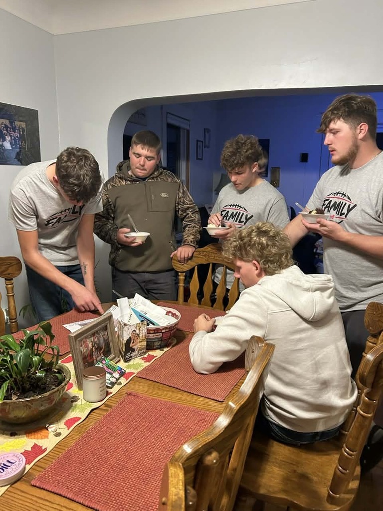 Five football players gather around a dining table, holding bowls and enjoying a meal together during their team dinner.