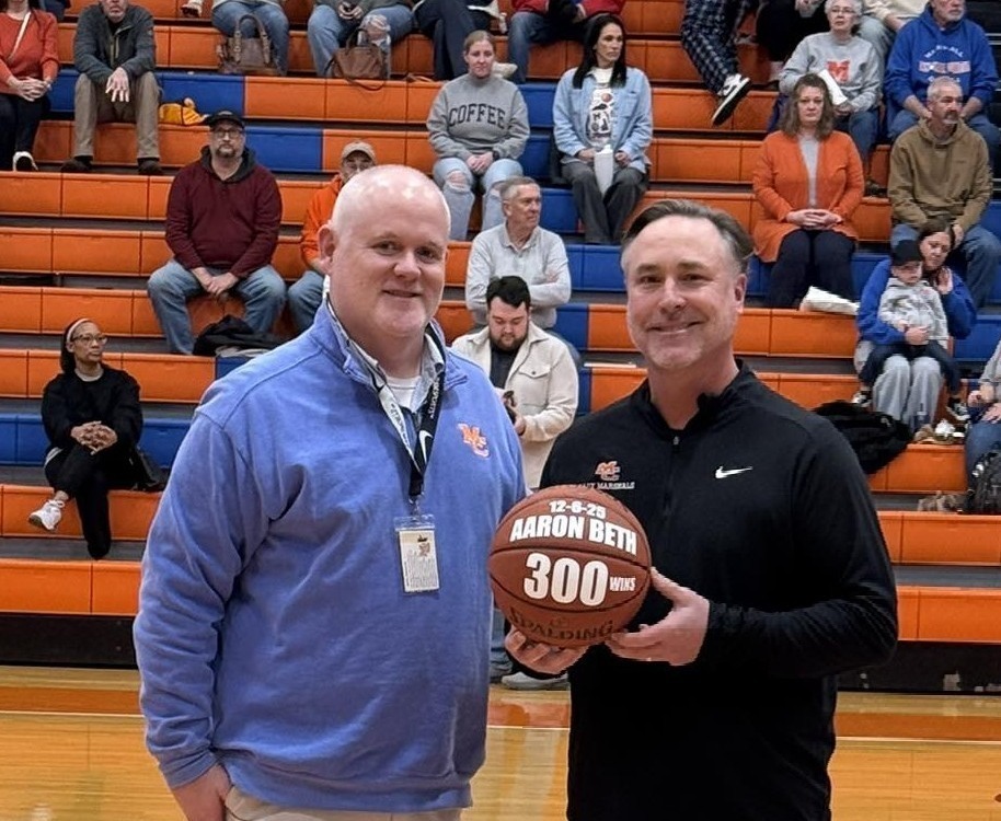 Photo of Aaron Beth holding 300th win basketball alongside MCHS principal Evan Merrick