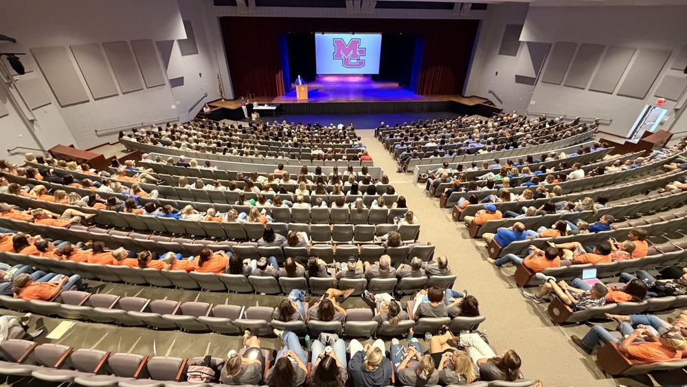 Wide shot of MC staff inside the Performing Arts Center listening to Supt. Thorpe on stage